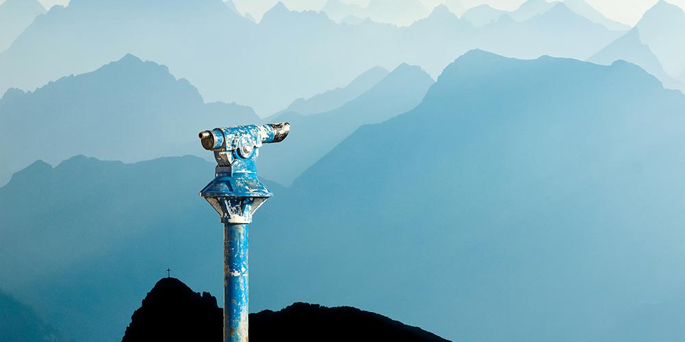 Public binoculars provide far view to distant blue mountain ranges silhouette in early Morning Sunlight